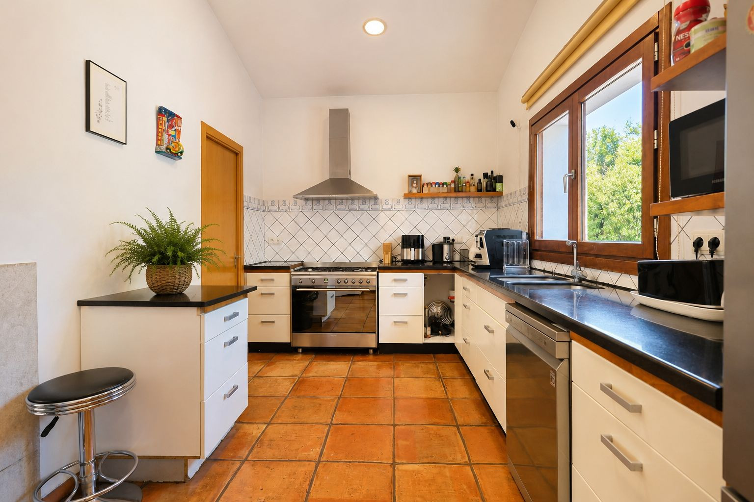 Functionele keuken met ambachtelijke terracotta vloeren, donkere werkbladen en grote houten ramen die overvloedig natuurlijk licht bieden.