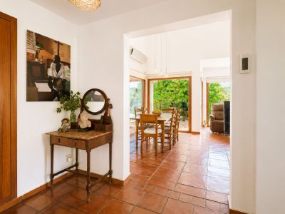 De lichte entree met traditionele terracotta vloer en vintage consoletafel opent naar een ruime eetkamer met grote ramen die uitkijken op de weelderige tuin.