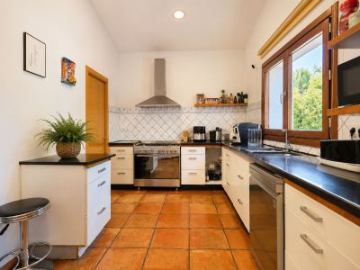 Functionele keuken met ambachtelijke terracotta vloeren, donkere werkbladen en grote houten ramen die overvloedig natuurlijk licht bieden.