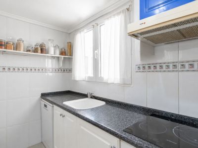 Aparte keuken met donker granieten aanrechtblad, witte spoelbak en inductiekookplaat. Witte tegelwanden met decoratieve rand en raam voor natuurlijk licht.