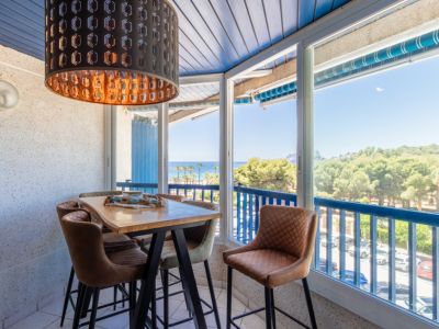 Beglaasde eethoek met hoge houten tafel, gestoffeerde barkrukken en opvallende zwarte hanglamp. Panoramisch uitzicht op zee, strand en dennenbos door grote ramen.