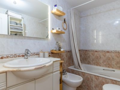 Complete badkamer met lichte tegels en decoratieve rand, geïntegreerde wastafel op marmeren blad, verlichte spiegel, ligbad met douchegordijn en bidet.