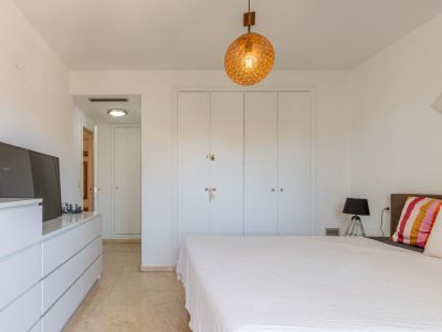 Hoofdslaapkamer met witte inbouwkasten, lichte marmeren vloer en een opvallende bolvormige hanglamp. Inclusief ladekast met tv en toegang tot gang.