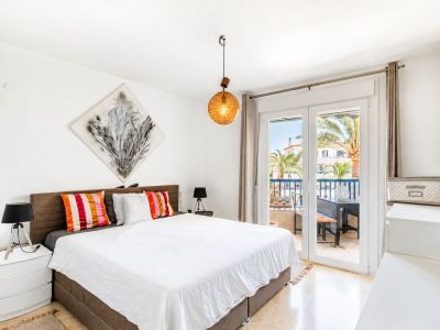 Lichte hoofdslaapkamer met directe toegang tot een privéterras, marmeren vloer en uitzicht op palmbomen. Een opvallende hanglamp en abstracte kunst sieren de ruimte.