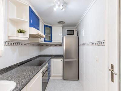 Praktische keuken met witte en blauwe kasten, donkere granieten werkbladen, een geïntegreerde inductiekookplaat en RVS-apparatuur. Natuurlijk licht valt binnen via het raam.