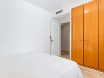 Slaapkamer met ruime, lichte houten inbouwkast en een bed met wit beddengoed. De kamer heeft een marmerlook vloer en een open deur naar een aangrenzende ruimte.