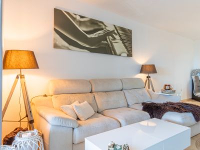 Woonkamer met lichte hoekbank, witte salontafel en twee vloerlampen met houten statief. Een groot kunstwerk van een piano siert de muur.