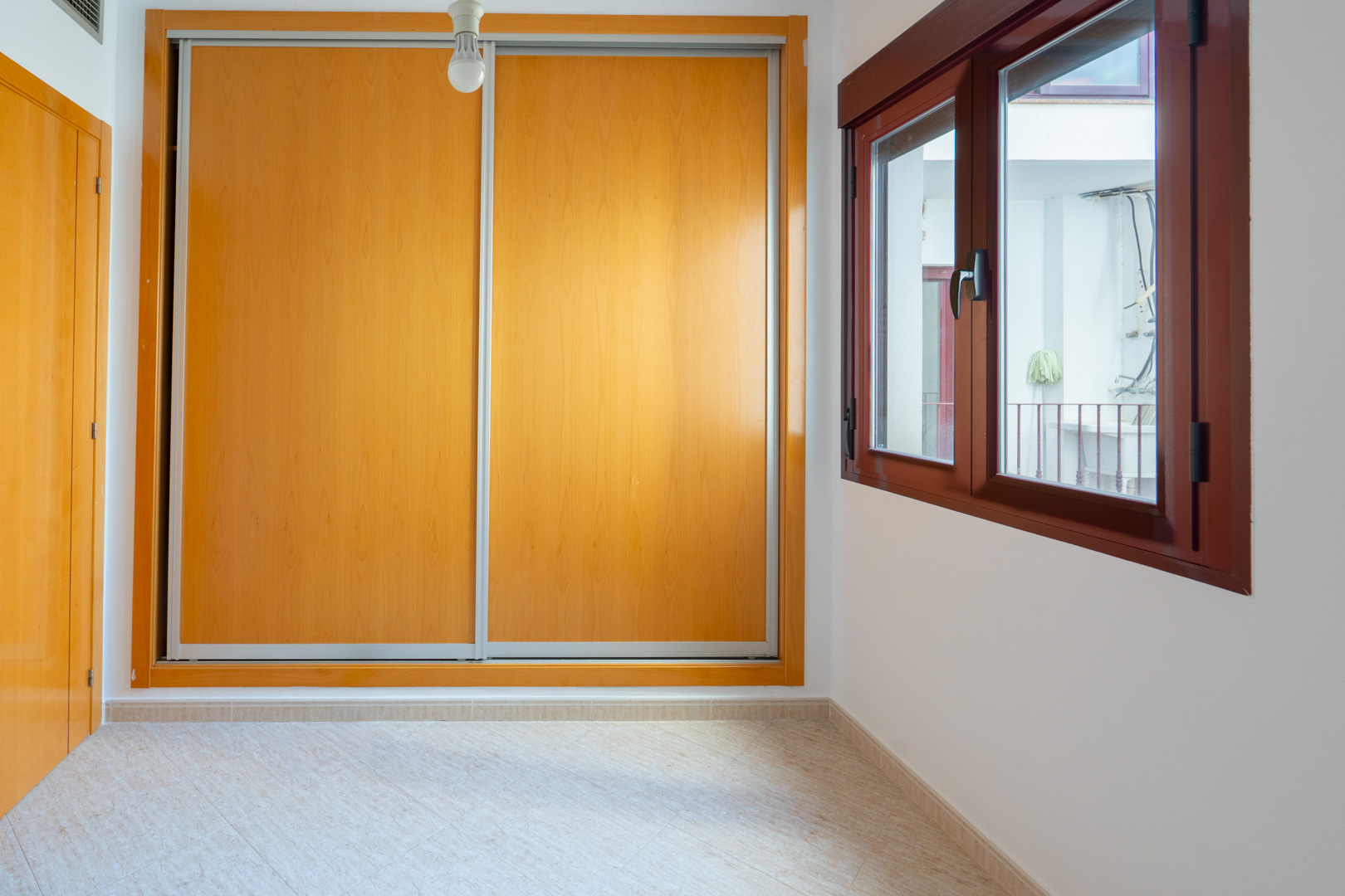 Slaapkamer met ruime inbouwkast met lichte houten schuifdeuren en donkerhouten raam dat uitkijkt op een binnenplaats.