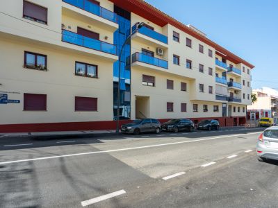 Exterieur van het woongebouw met lichte gevel, blauwe glazen balkons, ramen met bordeauxrode rolluiken en een verticaal glazen paneel.