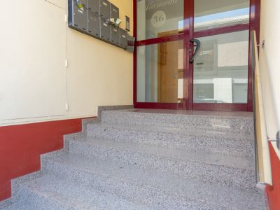 Graniteffect trappen leiden naar de hoofdingang van het gebouw, met een donkerrood omkaderde glazen deur, voorzien van 'Edificio Alameda 36', en een rij grijze brievenbussen aan de linkerwand.