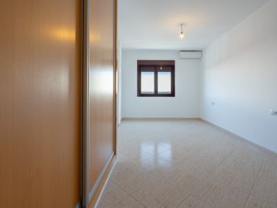 Lege kamer met lichte houten inbouwkast, diagonaal gelegde beige tegels en raam met uitzicht op daken. Een airconditioning unit is aanwezig.