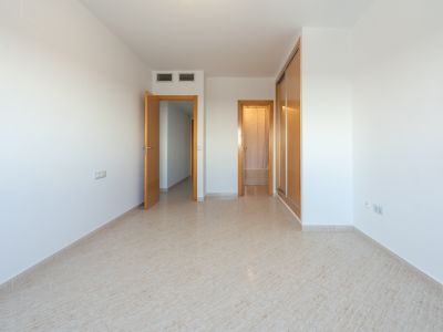 Lege kamer met lichte tegelvloer, een ingebouwde houten kledingkast met schuifdeuren en deuren naar aangrenzende ruimtes. Airconditioningroosters zijn zichtbaar.