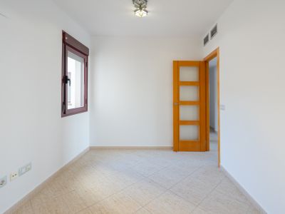 Lege kamer met witte muren, bordeauxrood kozijn en lichtbeige diagonale vloertegels. Een houten deur met glazen panelen en airco-roosters zijn aanwezig.
