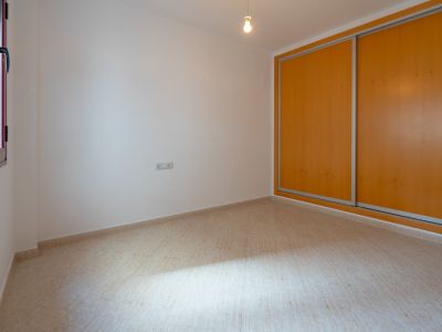 Lichte kamer met een ingebouwde kledingkast voorzien van twee lichte houten schuifdeuren en een beige tegelvloer. Een raam met donker kozijn zorgt voor natuurlijke lichtinval.