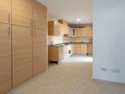 Ruime keuken met lichte houten kasten, gespikkelde granieten werkbladen en een geïntegreerde oven. Een grote bijpassende voorraadkast staat links op de beige tegelvloer.
