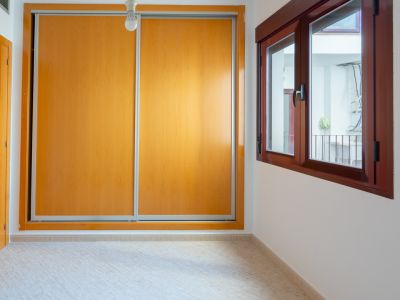 Slaapkamer met ruime inbouwkast met lichte houten schuifdeuren en donkerhouten raam dat uitkijkt op een binnenplaats.