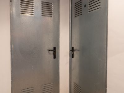 Twee grijze metalen deuren met boven- en onderroosters, één gemarkeerd met 'Benissa Denia' en de andere met nummer '5', op een gespikkelde granieten vloer.