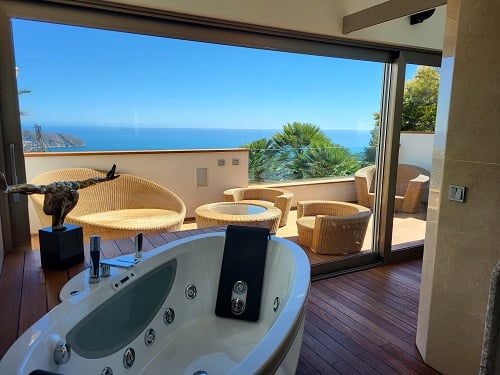 Binnenjacuzzi met houten vloer die uitkomt op een privéterras, ingericht met rotan meubilair en een panoramisch uitzicht op de Middellandse Zee biedt.