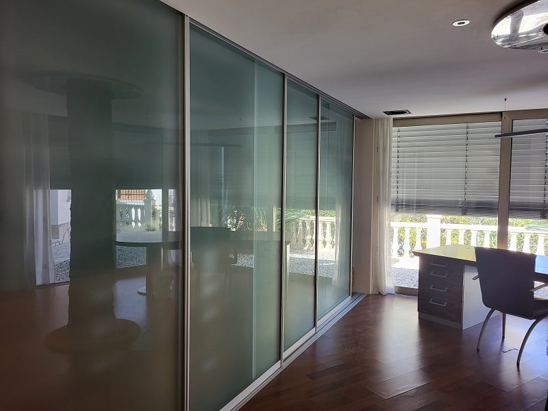 Kantoor of slaapkamer met elegante schuifdeuren van matglas, donkere houten vloer en een werkplek bij het raam met uitzicht op de balustrade.