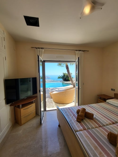 Lichte slaapkamer met eenpersoonsbedden en televisie, met directe toegang tot het terras. Geniet van het panoramische uitzicht op het infinity zwembad en de Middellandse Zee.