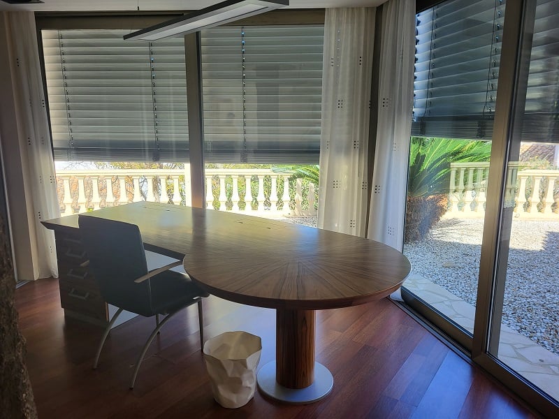 Ruime privékantoor met een groot houten bureau en parketvloer. De kamerhoge ramen bieden uitzicht op een balustrade en mediterrane tuin.