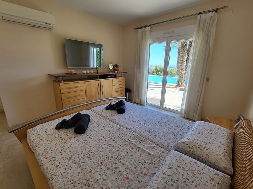 Slaapkamer met twee eenpersoonsbedden, wand-tv en directe toegang tot het terras met zwembad- en palmboomzicht. Voorzien van airconditioning.