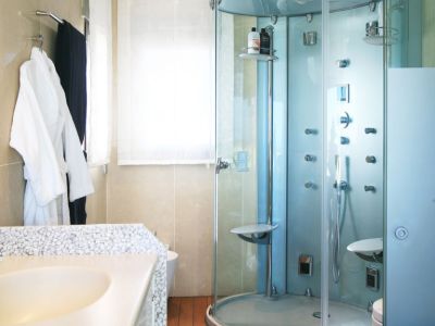 Badkamer met glazen douchecabine met meerdere jets, een wastafelblad met kiezeltextuur en warme houten vloer. Natuurlijk licht valt binnen via het raam.