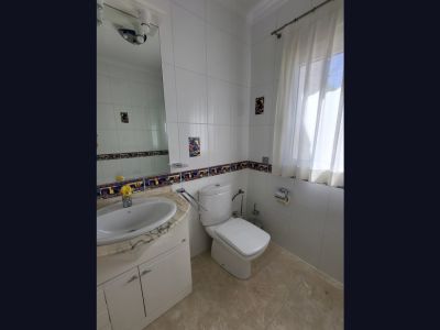 Badkamer met witte tegelwanden en decoratieve rand. Voorzien van een wastafel met licht marmeren blad, een toilet en een raam met doorschijnende gordijnen voor natuurlijk licht.