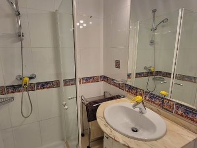Functionele badkamer met glazen douchecabine, wastafelmeubel met licht marmeren blad en verlichte spiegel. Witte tegels met decoratieve mediterrane rand.