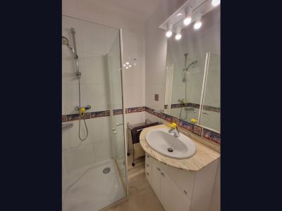 Functionele badkamer met inloopdouche met glazen scherm, wastafel in een licht marmeren blad en wit badmeubel. Witte wandtegels zijn voorzien van een decoratieve mediterrane rand.