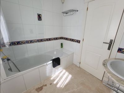 Functionele badkamer met wit ligbad, glazen douchescherm en witte tegelwanden met decoratieve rand. Voorzien van marmeren wastafel en natuurlijk lichtinval.