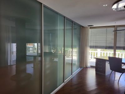 Kantoor of slaapkamer met elegante schuifdeuren van matglas, donkere houten vloer en een werkplek bij het raam met uitzicht op de balustrade.