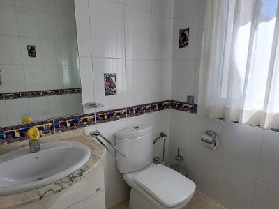 Lichte badkamer met witte wandtegels, een kleurrijke decoratieve rand en accentstukken. Voorzien van een marmeren wastafelmeubel met geïntegreerde wasbak, een modern toilet en een raam met vitrage.