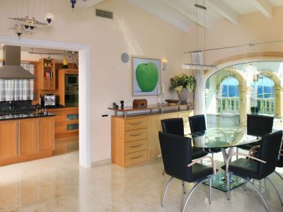 Lichte eetruimte met glazen tafel en zwarte stoelen, op gepolijste marmeren vloeren. Grote boogvensters bieden panoramisch zee- en bergzicht, grenzend aan een moderne keuken.