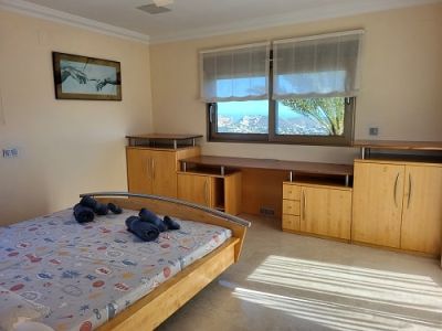 Lichte slaapkamer met licht houten bed, geïntegreerd bureau en kasten. De ramen bieden panoramisch uitzicht op de kust, waardoor de ruimte wordt gevuld met natuurlijk licht.