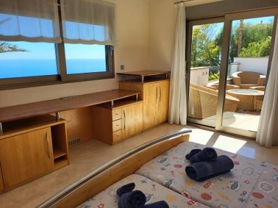 Lichte slaapkamer met twee eenpersoonsbedden, een geïntegreerd houten bureau en weids uitzicht op zee. Directe toegang tot een privéterras met zitmeubilair.