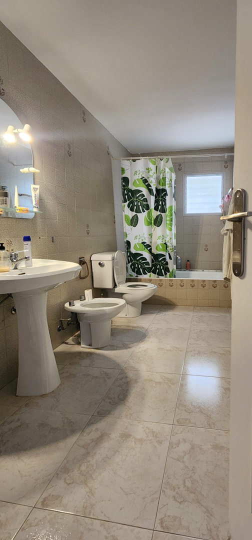 Functionele badkamer met lichte marmerlook vloertegels en beige wandtegels. Voorzien van een zuilwastafel, toilet, bidet en ligbad met douchegordijn en matglazen raam.