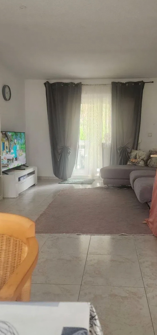 Ruime woonkamer met natuurlijk licht, voorzien van tegelvloeren, een comfortabele hoekbank en directe toegang tot een terras via glazen deuren met gordijnen.