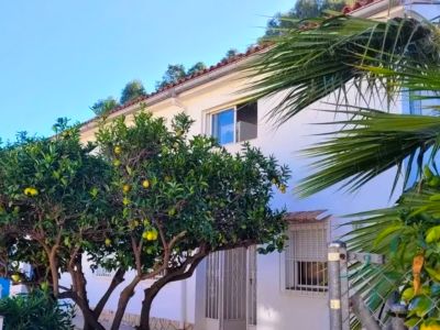 Buitenaanzicht van de witte villa met pannendak en citrusbomen vol gele vruchten. Een entree en ramen op de begane grond en verdieping zijn zichtbaar.