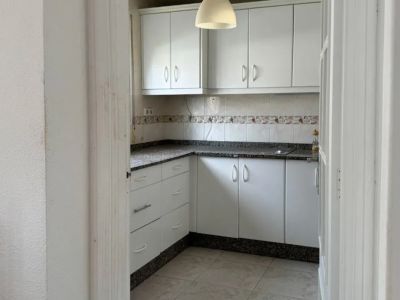 Functionele keuken met witte kasten, een donker gespikkeld granieten aanrechtblad en betegelde achterwand. Een hanglamp verlicht de ruimte, klaar voor modernisering.
