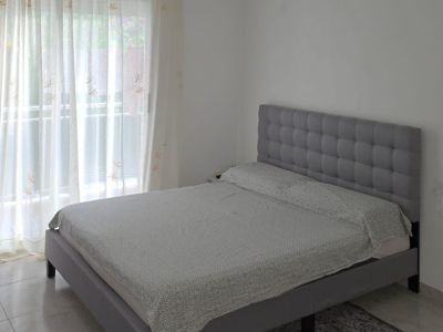 Tweepersoons slaapkamer met grijs gestoffeerd bed en gecapitonneerd hoofdbord, tegelvloer en veel natuurlijk licht van het raam met terras toegang.