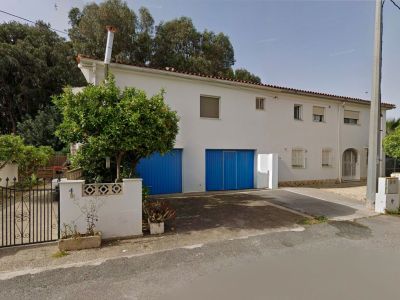 Voorgevel van de halfvrijstaande villa, met een witte gevel, twee opvallende blauwe garagedeuren en een sinaasappelboom bij het smeedijzeren toegangshek.