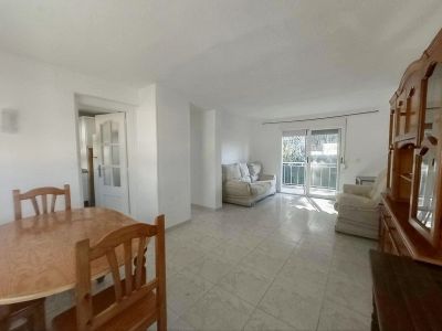 Zicht op de lichte woon-eetkamer met een ovale houten tafel, tegelvloeren en een grote houten vitrinekast. Glazen schuifdeuren openen naar een balkon, waardoor de ruimte natuurlijk licht ontvangt.