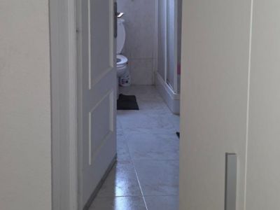 Zicht op een badkamer met lichte tegelvloer en witte wandtegels met decoratieve rand. Voorzien van een toilet, douchecabine en natuurlijk licht via een raam.