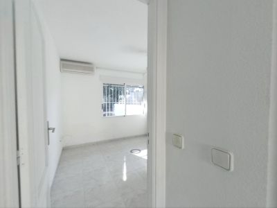 Zicht op een lege kamer met lichte tegelvloer, witte muren en een airconditioningunit. Het raam met tralies zorgt voor natuurlijk daglicht.