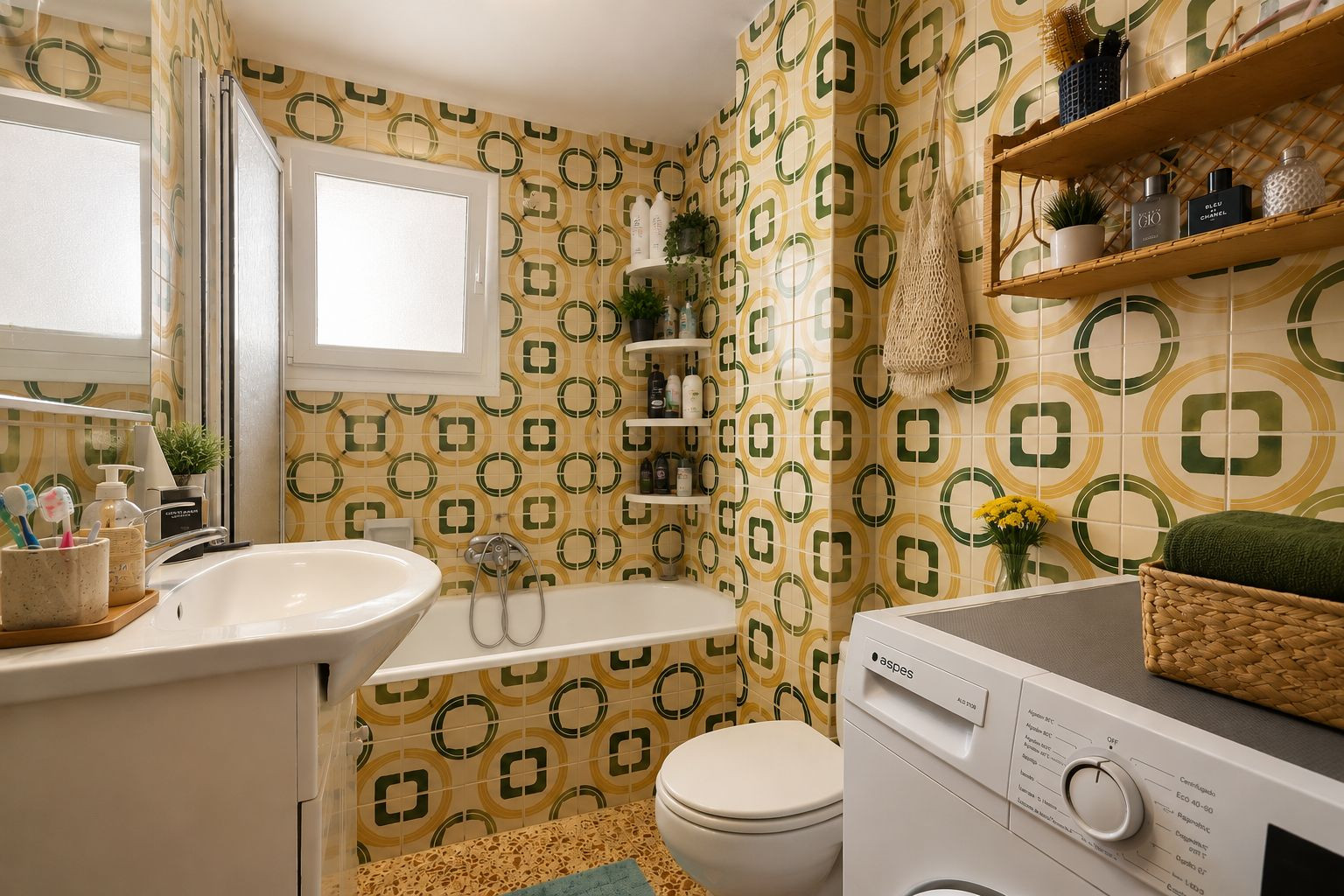 De complete badkamer heeft opvallende geel-groene geometrische tegels, een wastafelmeubel, een ligbad met douchescherm en een geïntegreerde wasmachine, verlicht door een matglazen raam.
