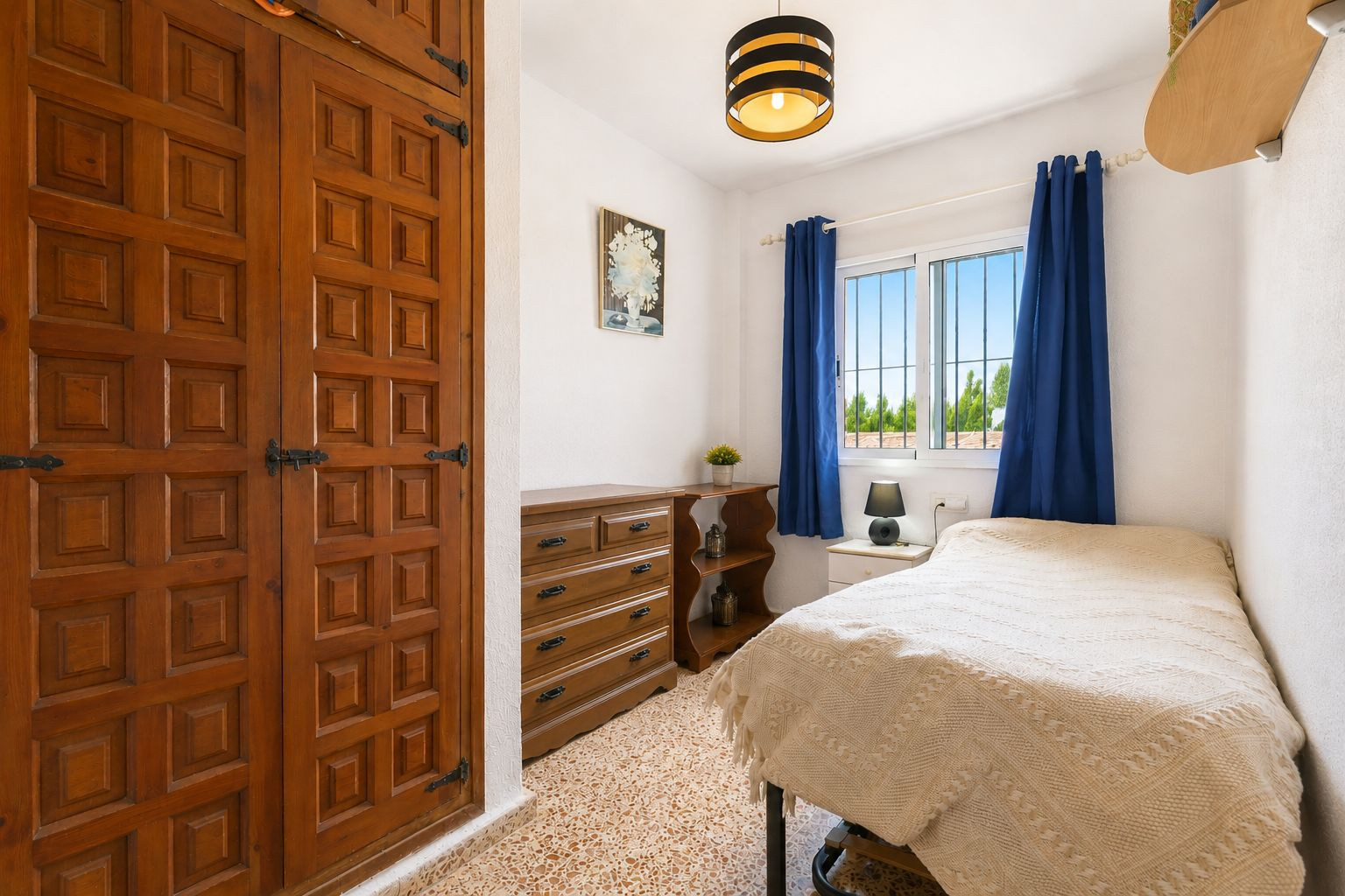 Gezellige slaapkamer met opvallende ingebouwde houten kledingkast, decoratieve panelen en zwart beslag. Natuurlijk licht door raam met blauwe gordijnen en uitzicht op groen.