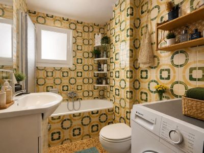 De complete badkamer heeft opvallende geel-groene geometrische tegels, een wastafelmeubel, een ligbad met douchescherm en een geïntegreerde wasmachine, verlicht door een matglazen raam.
