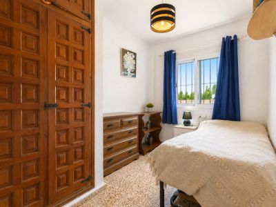 Gezellige slaapkamer met opvallende ingebouwde houten kledingkast, decoratieve panelen en zwart beslag. Natuurlijk licht door raam met blauwe gordijnen en uitzicht op groen.