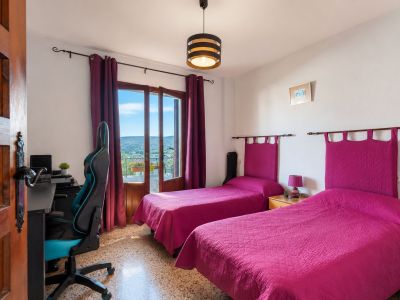Lichte slaapkamer met twee eenpersoonsbedden, fuchsia hoofdeinden en directe toegang tot een balkon met berguitzicht. Voorzien van een bureau en terrazzovloer.